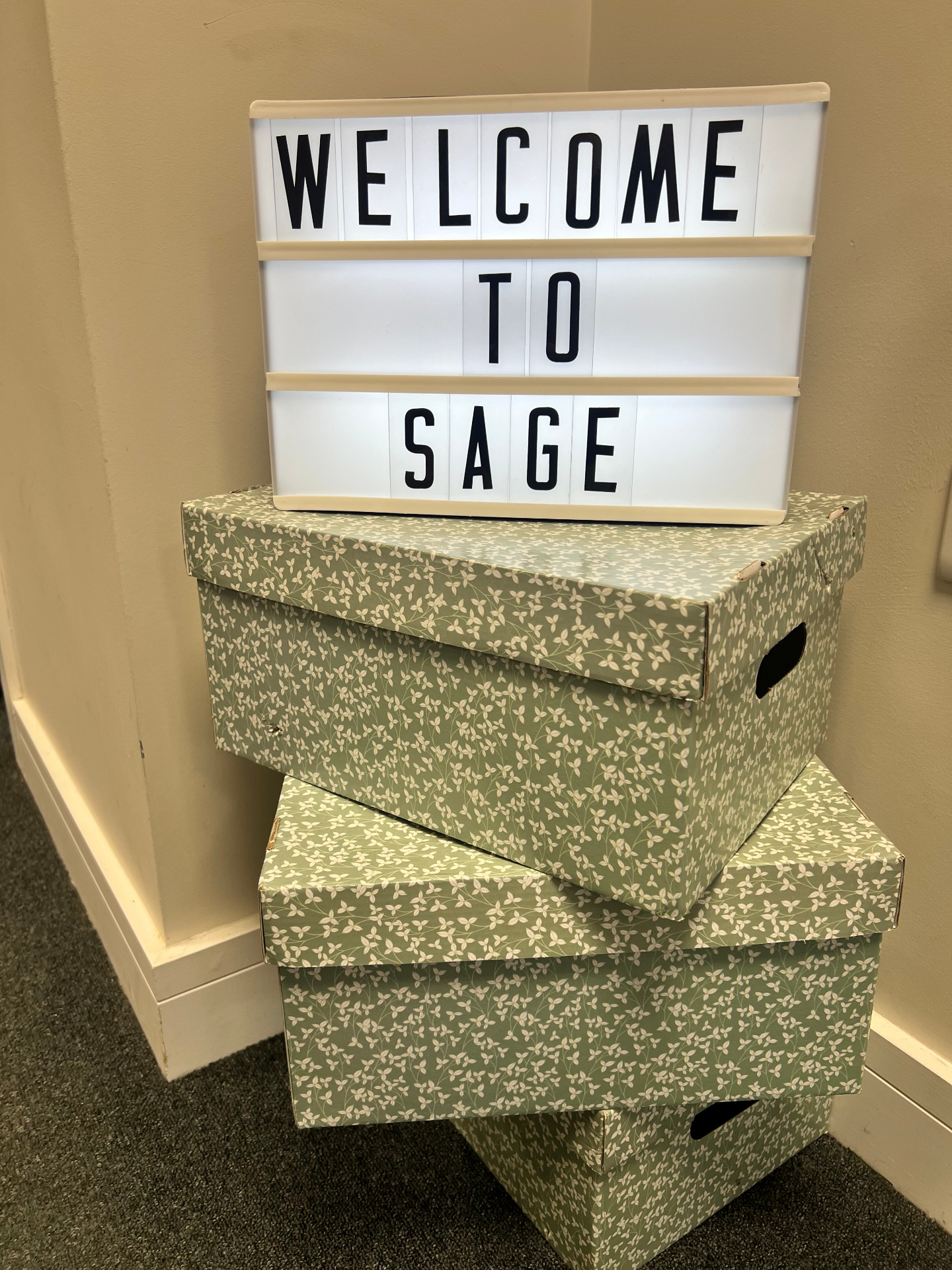 A lightbox sign reading 'Welcome to Sage' displayed on decorative storage boxes